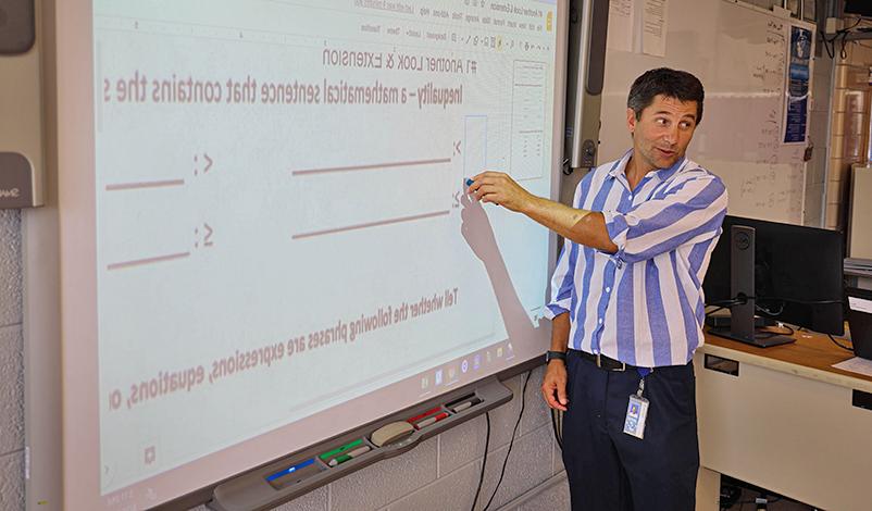 Terry standing in front of a projector, pointing at a math problem on the board